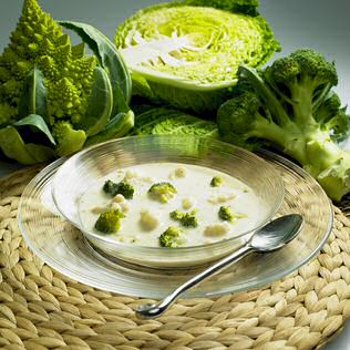 Een kom geroosterde bloemkoolsoep met broccoliroosjes: op de achtergrond romanesco of groene torentjesbloemkool, savooikool en broccoli
