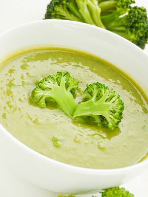 Een kom lekker verse broccolisoep volgens een recept van Jeroen Meus en Ons Kookboek met extra broccoliroosjes geserveerd